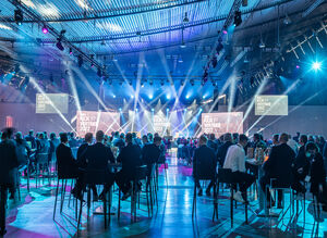 Kickoff Abendveranstaltung mit sitzenden Gästen, die zu einem Redner auf der Bühne blicken