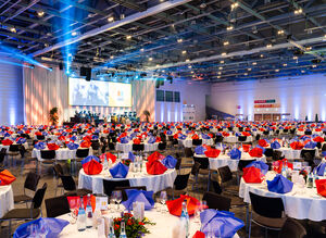 Gedeckte Tische im Vordergrund mit blauen und roten Servietten, Bühne im Hintergrund