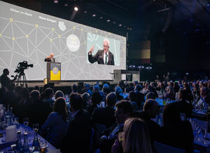 Gäste sitzen an Tischen und blicken auf die Bühne zu Winfried Kretschmann