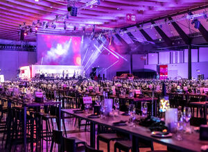 Leere Messehalle mit gedeckten Tischen und einer großen Bühne im Hintergrund