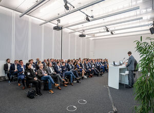 Seitlicher Blick auf sitzende Gäste von vorne und zwei Redner an einem Pult von hinten.