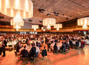 Gäste in Abendgarderobe essen an runden Tischen, Location ist mit Kronleuchtern geschmückt