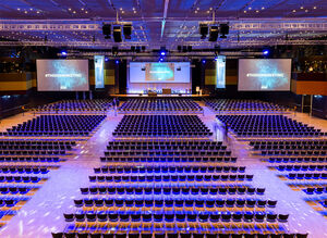 Bestuhlte leere Location mit großer Bühne und drei Leinwänden im Hintergrund