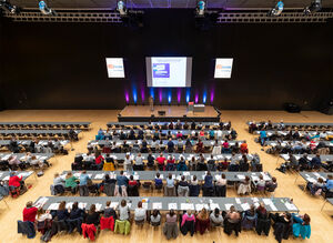 Vogelperspektive auf einen Kongress mit sitzenden Gästen und Sprecher auf einer Bühne